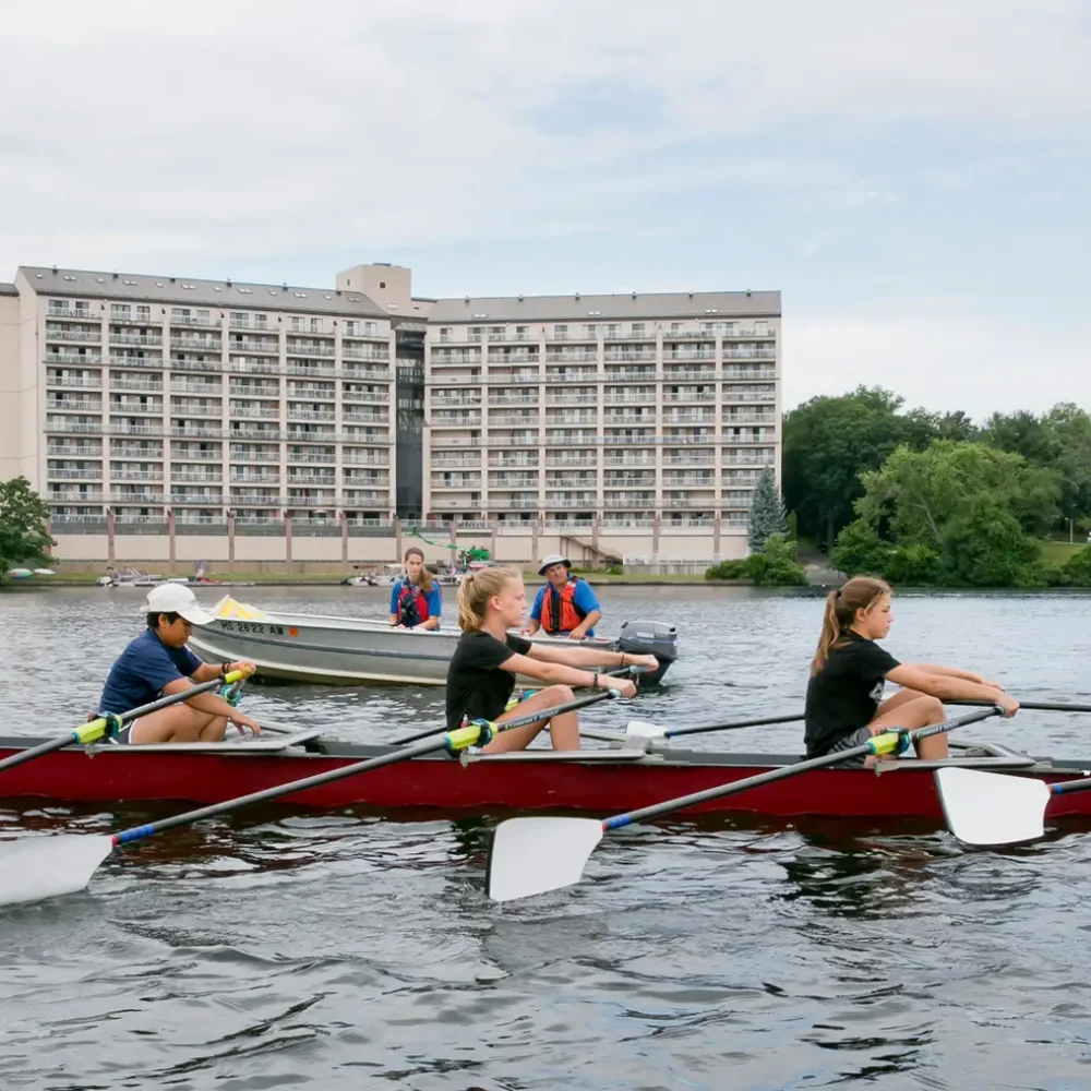 Kids in a rowing shell while a coach instructs from a motorboat